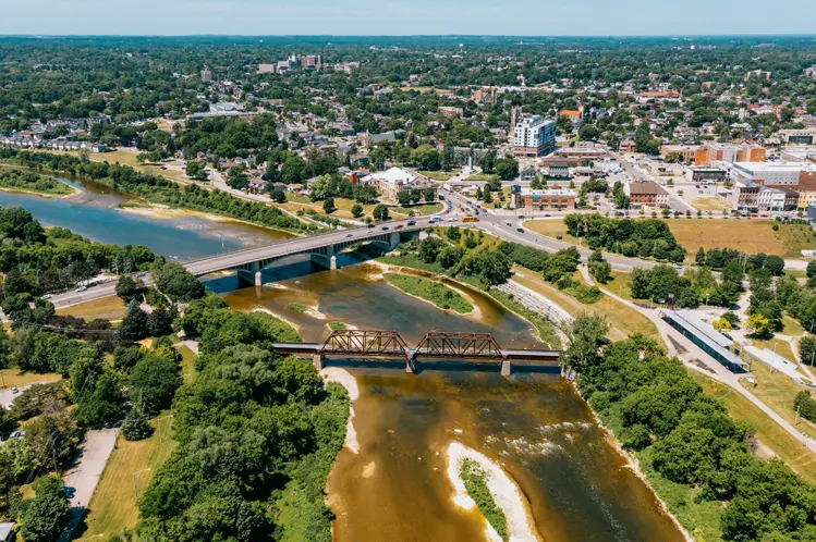 Aerial view of Brantford with Lorne Bridge and rail bridge spanning the Grand River, surrounded by greenery and urban buildings.