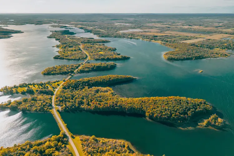 화창한 날 숲이 우거진 섬들을 지나는 롱솔트 파크웨이의 구불구불한 도로, 반짝이는 호수가 풍경을 가로질러 펼쳐져 있습니다.