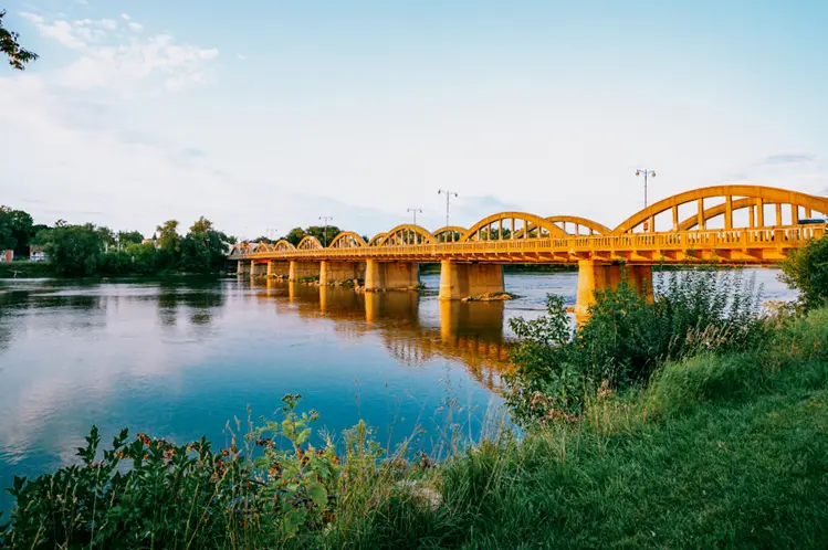  カレドニアのアーガイル ストリート橋の湾曲したコンクリートのアーチが夕日に輝き、前景の緑とともに静かな水面に映っています。