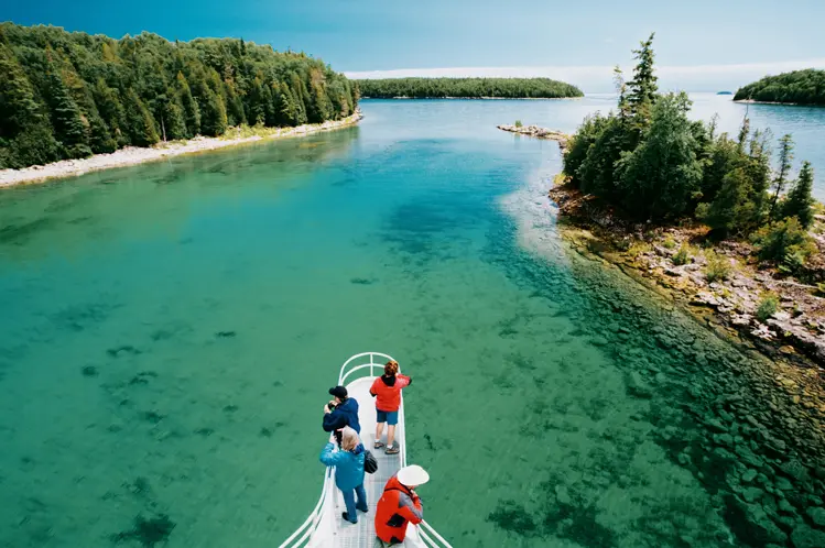 Visitors on a boat cruise through clear turquoise waters near Tobermory on the Bruce Peninsula, surrounded by forested islands.