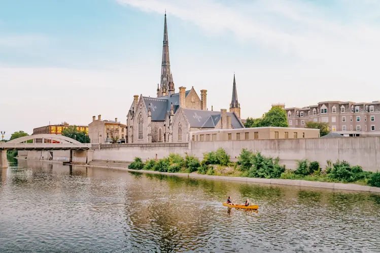 Eine Kanufahrt auf dem Grand River in der Innenstadt von Cambridge, Ontario, vorbei an historischen Gebäuden und Kirchtürmen im Abendlicht.