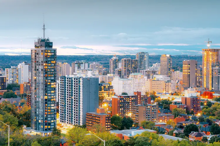 Die Skyline von Hamilton, Ontario, leuchtet zur blauen Stunde, mit Hochhäusern und Bürotürmen, die sich vor einem Abendhimmel abheben.