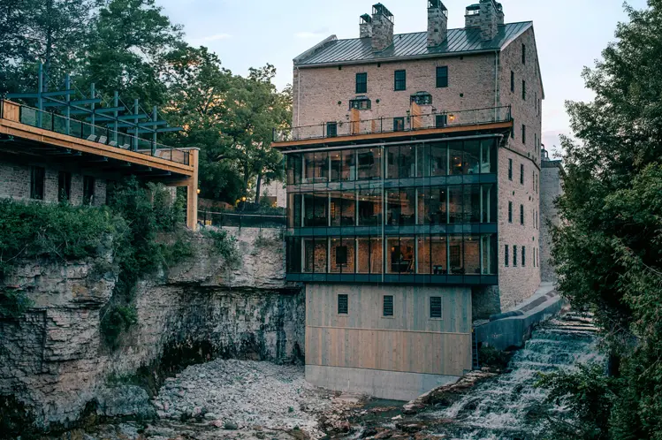 Die historische Elora Mill aus Stein mit einem modernen Glasanbau thront über der Elora-Schlucht und bietet Aussicht auf die felsigen Klippen und das herabstürzende Wasser.