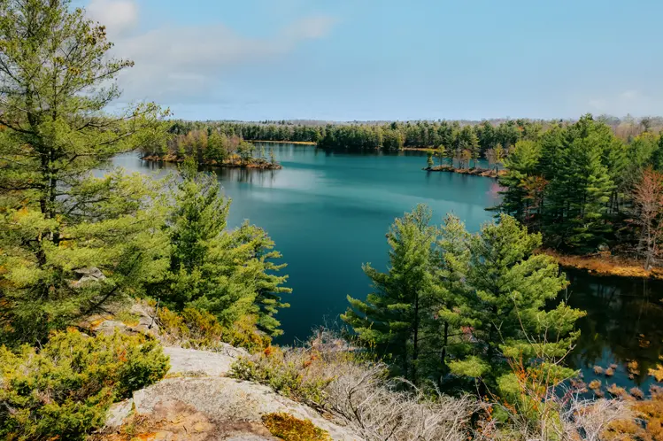 曇り空の春の日に、フロンテナック州立公園の岩だらけの地形と深い松林に囲まれた湖の景色。