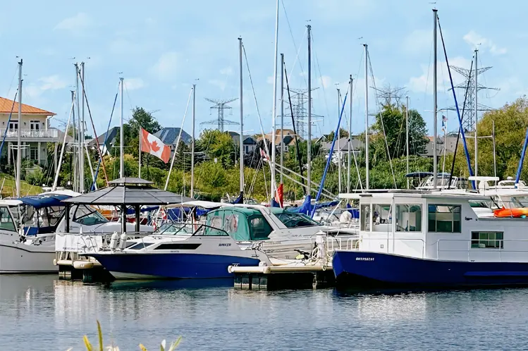 Boats docked at a marina in Clarington, Ontario, with sailboat masts rising above the water and a Canadian flag waving in the breeze.