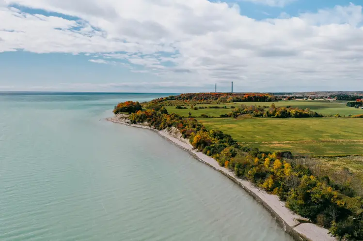 Türkisfarbenes Wasser entlang der Küste von Port Hope in Northumberland, mit üppigem Grün und einem bewölkten blauen Himmel darüber.