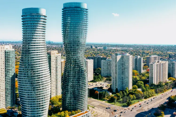 ミシサガのアブソリュート ワールド コンプレックスの航空写真。晴れた日に周囲の高層ビルの上にそびえ立つ、曲線を描くモダンなツインタワーが映えます。