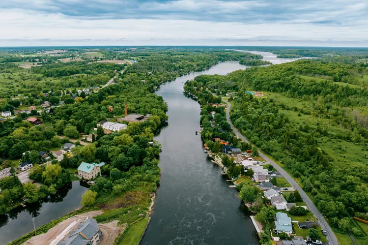 Aerial view of Hastings, Ontario, showing a winding river lined with homes and trees, stretching through a lush, green rural landscape.