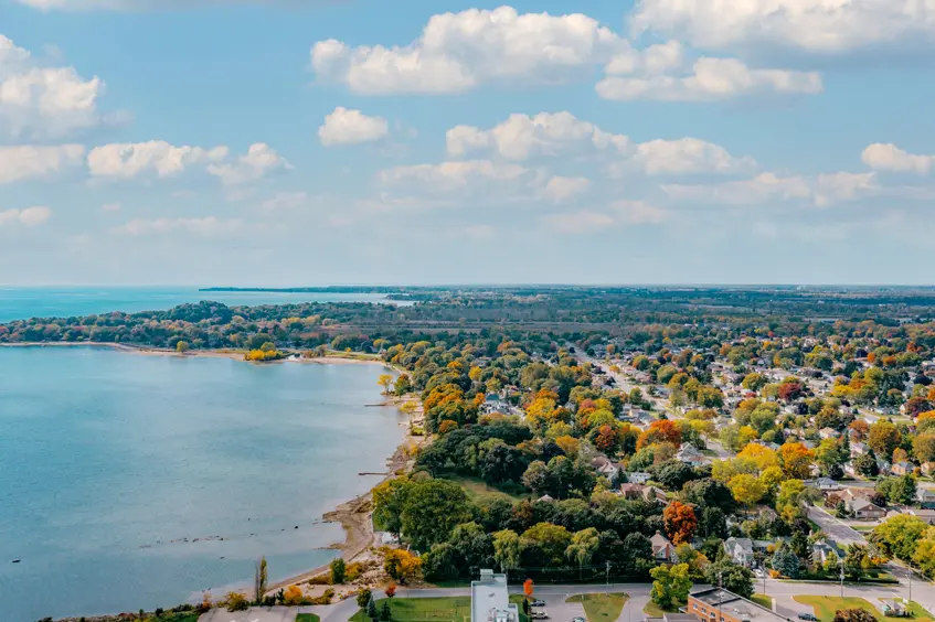 Vue aérienne du parc Knoll Lakeview et du lac Érié, à Port Colborne, montrant les arbres au feuillage automnal sous un ciel lumineux rempli de nuages.