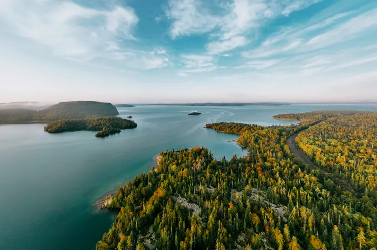  맑은 여름날, 로스포트 근처 슈피리어 호에 있는 섬과 숲이 우거진 해안선을 공중에서 본 모습. 고요하고 푸른 물과 탁 트인 하늘이 보입니다.