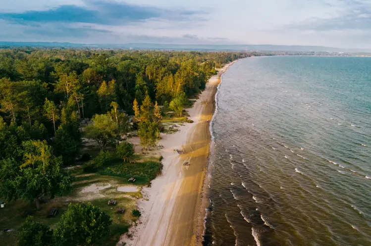 ワサガ ビーチの航空写真。広い砂浜、ビーチに隣接する森林公園、パステルカラーの夕焼け空の下の穏やかな波が見えます。