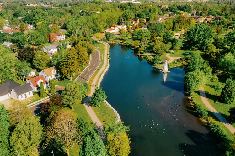  Vista aérea del parque Wellington en Simcoe, con un río sinuoso, árboles verdes y una estructura blanca estilo faro en el agua.