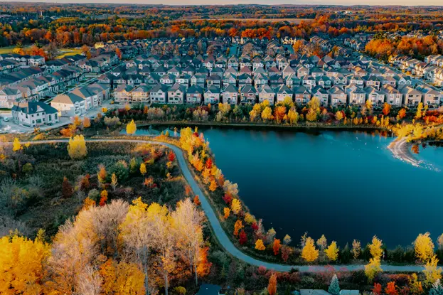  Vista aérea de un suburbio de Woodbridge con filas de casas perfectamente alineadas, un pequeño lago, senderos sinuosos y coloridos árboles otoñales en un día de otoño.