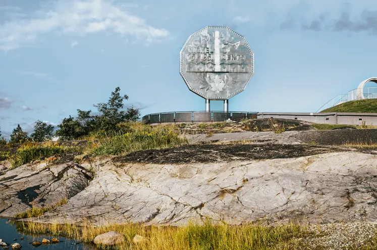 Réplique argentée géante d’une pièce de cinq cents au-dessus d’un terrain rocheux et d’un étang à Terre dynamique, à Sudbury, un jour d’été.