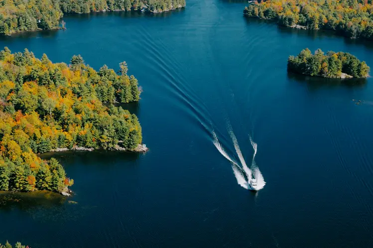 Two boats cruising on a blue lake leaving white trails, surrounded by forested shoreline in Orillia and Lake Country.