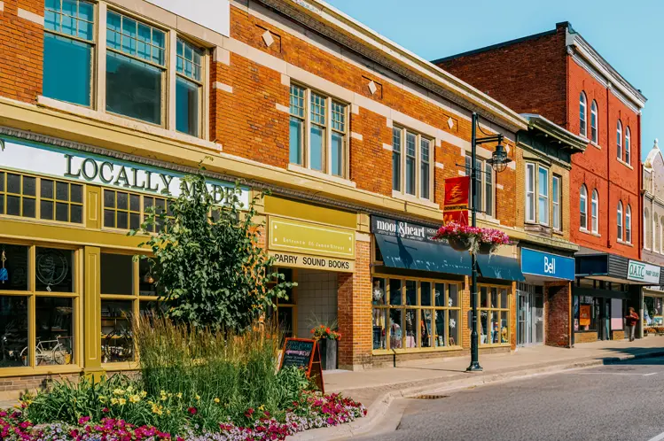 晴れた夏の日、パリーサウンドのダウンタウンにあるカラフルな歴史的な店舗、歩道沿いには明るい花壇や吊るしバスケットがあります。
