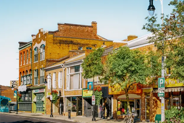 Façades historiques colorées au centre-ville de St. Catharines, avec des arbres et des parterres de fleurs, un jour d’été ensoleillé.