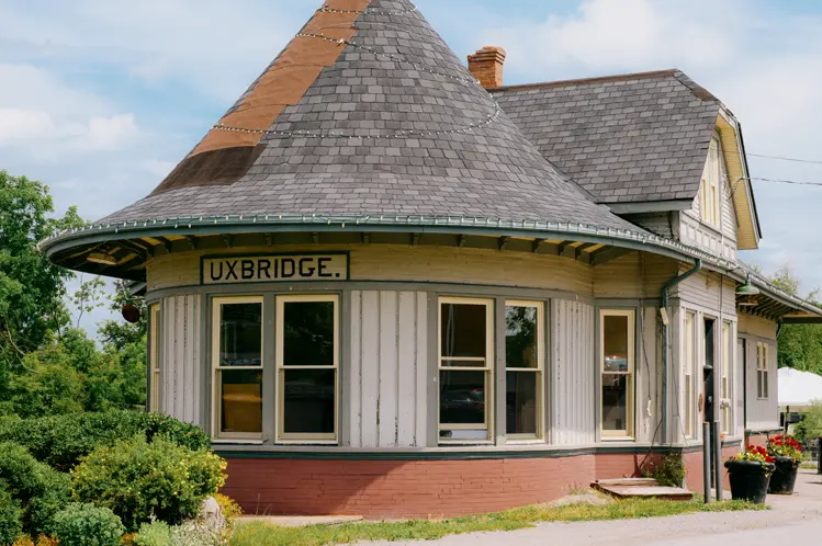 夏の日にプランターに囲まれた、丸い塔のような屋根、クリーム色のサイディング、大きな窓を備えた歴史的なアクスブリッジ駅。