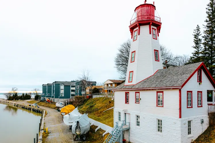 曇りの日のヒューロン湖岸沿いにある白と赤の八角形のキンカーディン灯台。近くにはボートが保管されています。