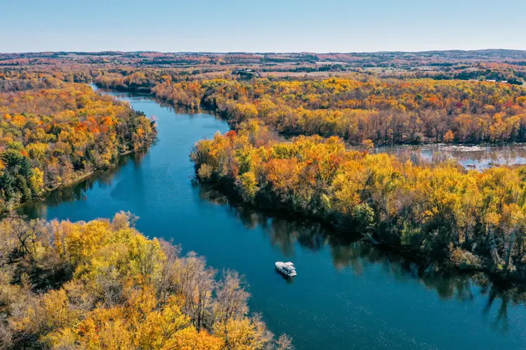 A calm river winding through a tree-filled landscape in Kawartha Lakes, bursting with vibrant fall foliage.