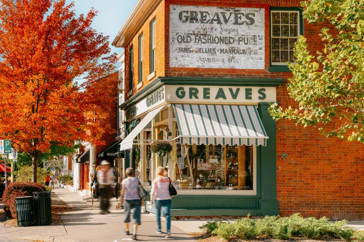 ナイアガラ・オン・ザ・レイクの賑やかなクイーン・ストリートにあるグリーブス・ジャムのショップと色とりどりの秋の木々を通り過ぎて散歩する訪問者。