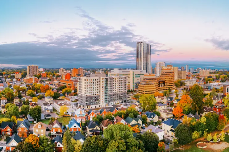 Kitchener cityscape at sunset, with a blend of tall modern buildings and residential homes under a dramatic, cloud-streaked sky.