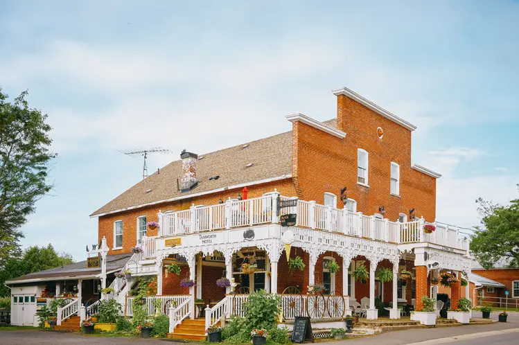 La fachada de ladrillo rojo del Hotel Tamworth, con encantadores balcones envolventes blancos y plantas colgantes en un día nublado de verano.