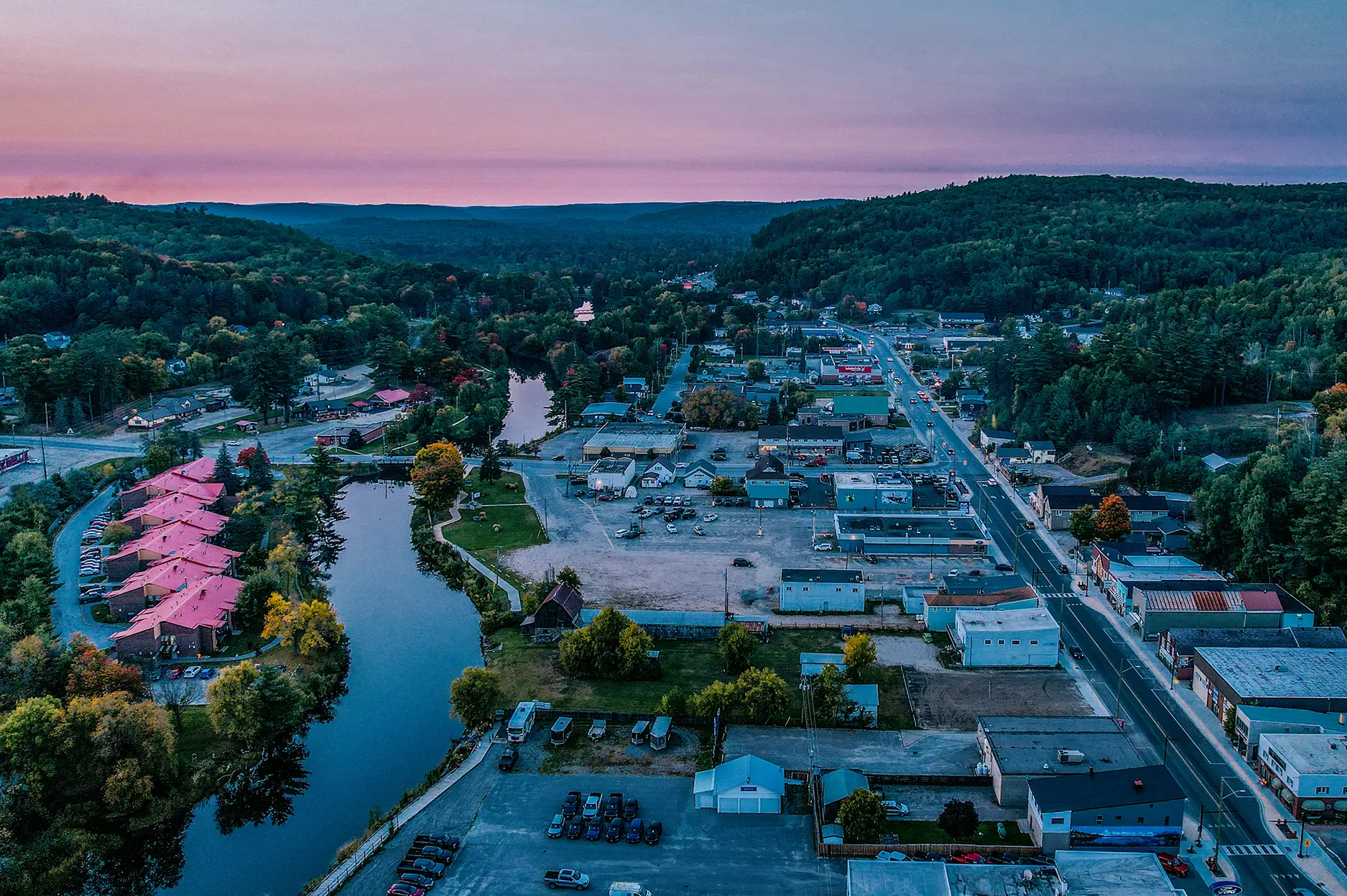 Vista aérea de Hastings, Ontario, que muestra un río sinuoso bordeado de casas y árboles, que se extiende a través de un exuberante paisaje rural verde.