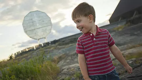 A child smiles in the foreground of the Big Nickel dominating the sky behind him.