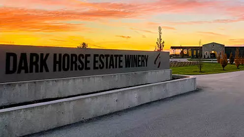 Dark Horse Estate Winery sign with the winery building in the distance during a sunset.