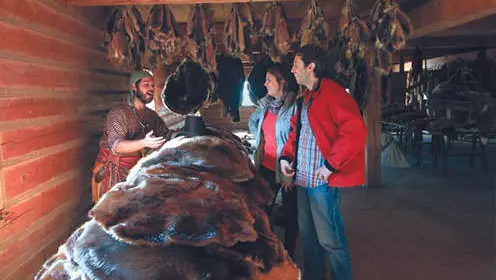 Un commerçant de fourrures expose ses marchandises à quelques visiteurs dans un poste de traite