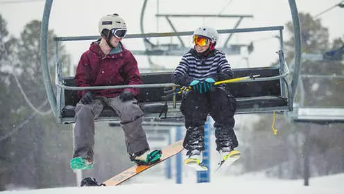 A snowboarder and skiier share a chairlift to the top of the mountain