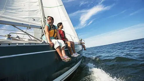 Sailors sit on the side of a sailboat as they enjoy a sunny day