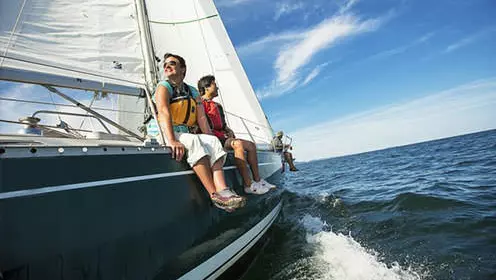Sailors sit on the side of a sailboat as they enjoy a sunny day