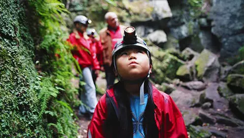 Child with hard hat and head lamp looking up in cave