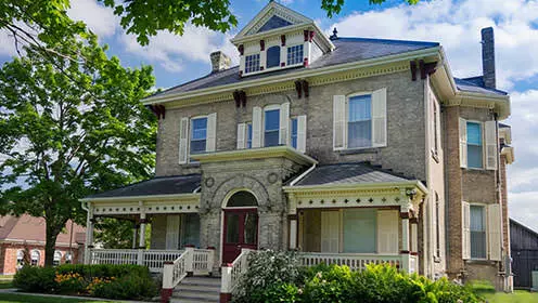 Ein großes viktorianisches lederfarbenes Backsteinhaus, umgeben von Bäumen und gepflegten Grundstücken.