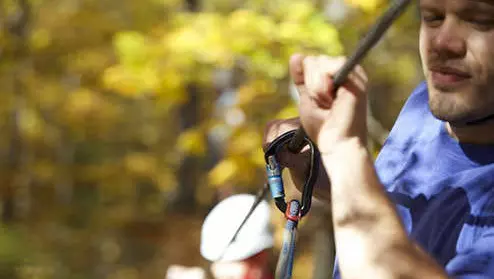 Ein Abenteurer schnappt sich einen Sicherheitshaken beim Ziplining durch einen Wald