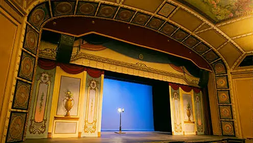 A smaller indoor theatre where the stage is surrounded with ornate tiles and paintings. A single floor lamp sits in the middle of the stage.