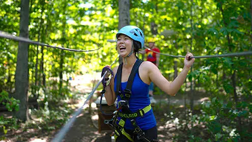 森の中のジップラインに取り付けられたハーネスを着た女性が笑う。
