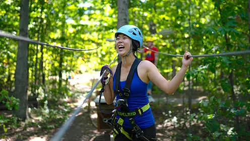 森の中のジップラインに取り付けられたハーネスを着た女性が笑う。