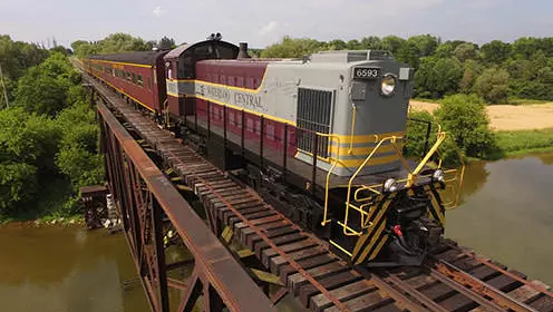 Ein großer Traditionszug überquert eine Eisenbahnbrücke über einen breiten Fluss.