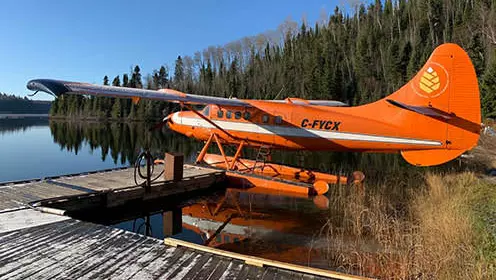 An orange seaplane tied to the dock on the shores of a lake.