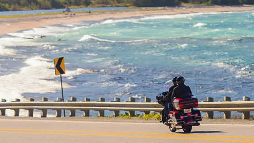 A couple on a motorcycle riding along a road next to a lake 