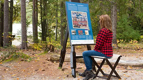 A seated woman in front of a painting on a tripod 