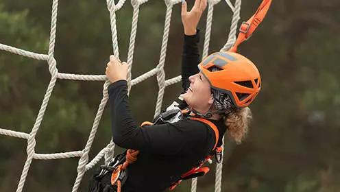 A close up of a woman wearing a helmet and a harness while grabbing onto a large net made from rope.