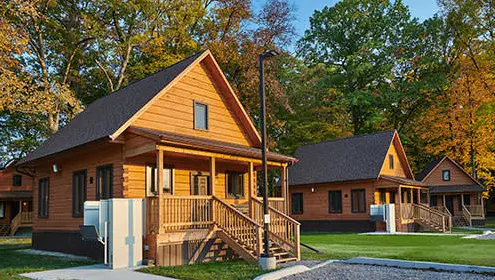 A row of newly built accessible cabins each with their own gravel parking spots and surrounded by grass and trees. 