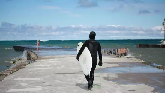 Surfer holding surf board walking towards a lake