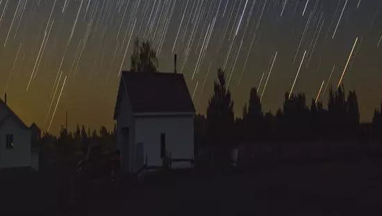 A dramatic show of stars illuminates the dark sky over a rural farm scene