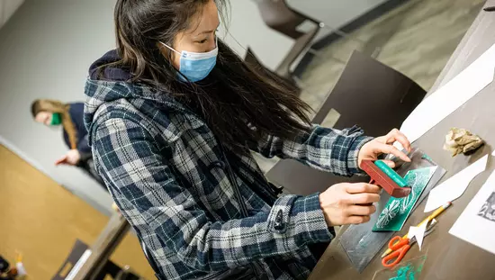 Young woman sitting at table with tools crafting a green design on small white card