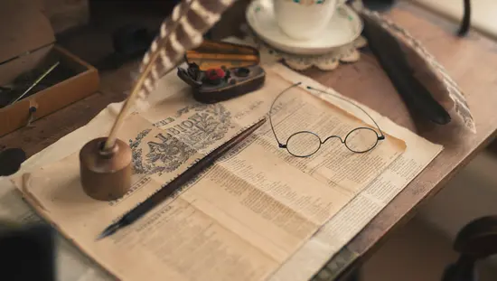 Table avec tasse et soucoupe de porcelaine à côté de la première page d'un journal historique avec des stylos et des lunettes de lecture d'époque sur le dessus.